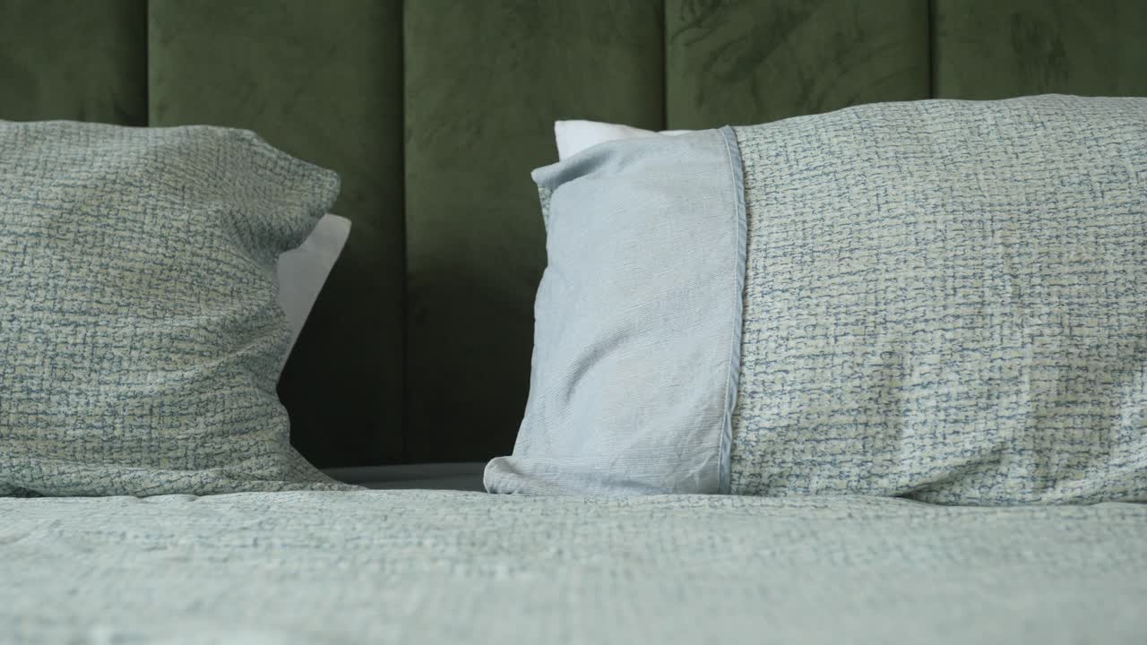 closeup de una cabecera de terciopelo verde con dos almohadas en una cama