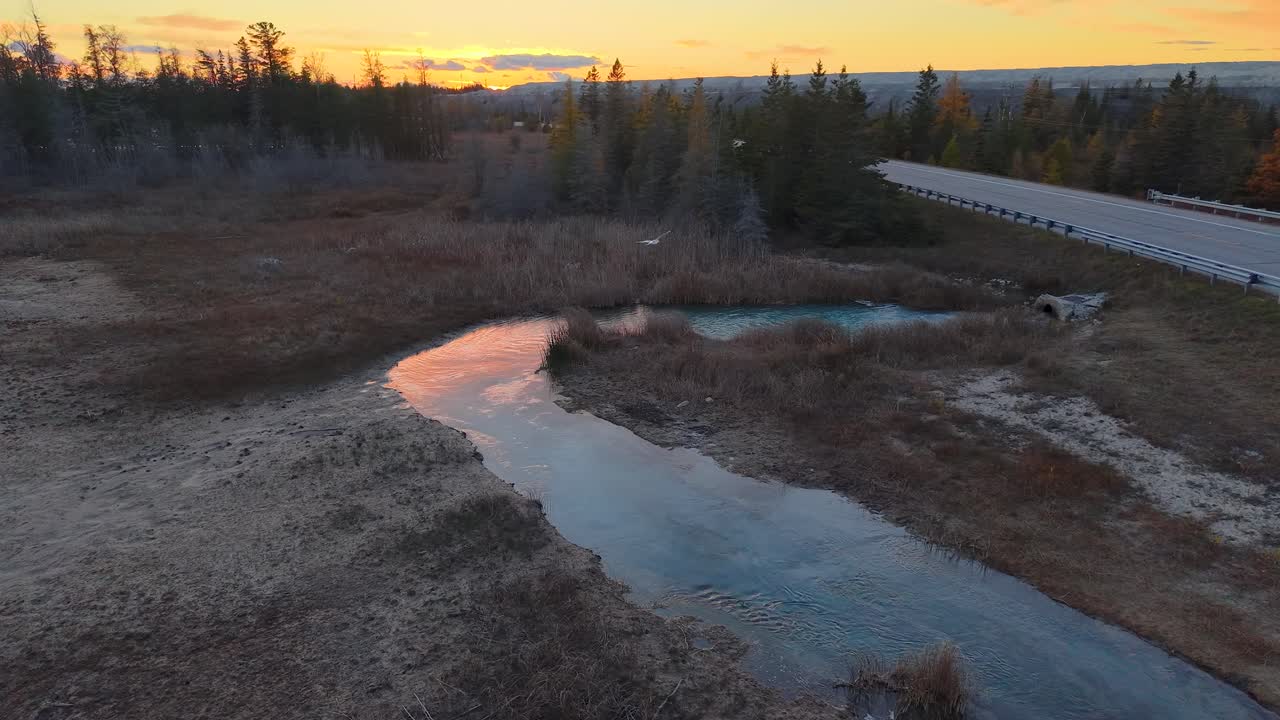 Aerial footage of a winding stream cutting through a grassy marsh with a forested horizon at sunset