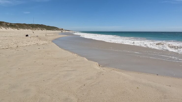 Handaufnahme, die Wellen zeigt, die am Strand mit Dünen und Angelruten brechen.
