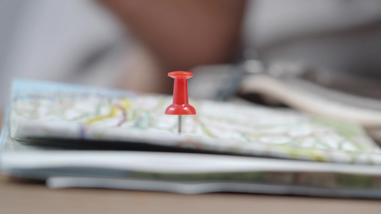 Hand Placing Red Pushpin on a Map to Mark a Travel Destination