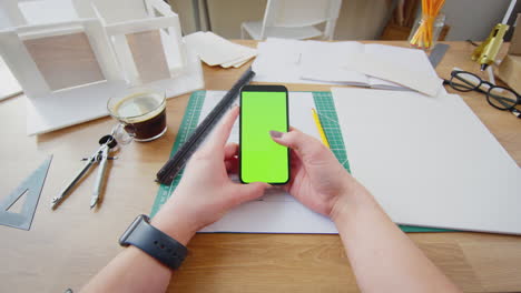 pov shot of female architect working in office on plans for new building using mobile phone