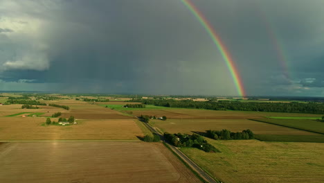 Wunderschöne-Aufnahme-Von-Zwei-Regenbögen-Am-Horizont,-Umgeben-Von-Einem-Feld,-Einer-Straße-Und-Der-Natur