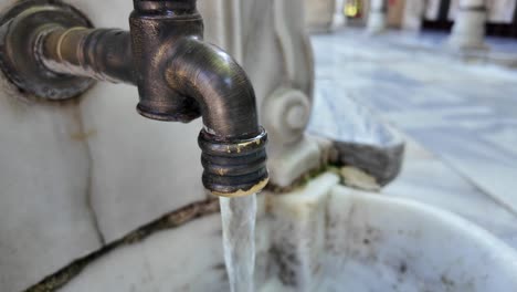 close-up of an old brass faucet with water flowing into a marble basin