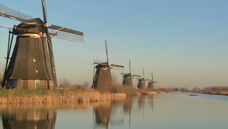 windmills line up perfectly along a canal as a small boat crosses in the distance