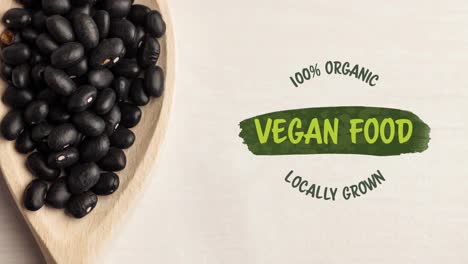 Animation-of-vegan-food-text-in-green-over-fresh-organic-black-beans-in-wooden-bowl