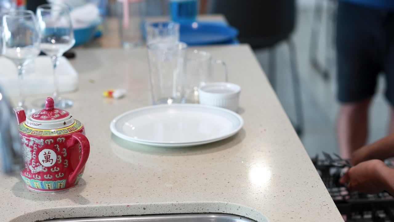 A person places a spoon into a dishwasher in a bright kitchen setting