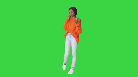 pretty african american woman in bright jumper talking on the phone and gesturing emotionally on a green screen, chroma key