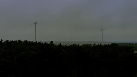 Imágenes-Aéreas-Cerca-De-Molinos-De-Viento-Cerca-De-árboles-Altos,-Condiciones-Climáticas-Nubladas-En-El-Horizonte,-Video-De-Grabación-De-Drones-4k