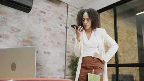 Ocupada-Empresaria-Birracial-Hablando-Por-Teléfono-Inteligente-Y-Usando-Una-Computadora-Portátil-En-La-Oficina,-En-Cámara-Lenta