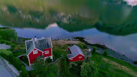 A-picturesque-red-house-and-barn-in-Flam,-Norway-then-tilt-up-aerial-to-reveal-a-cruise-ship-on-the-fjord