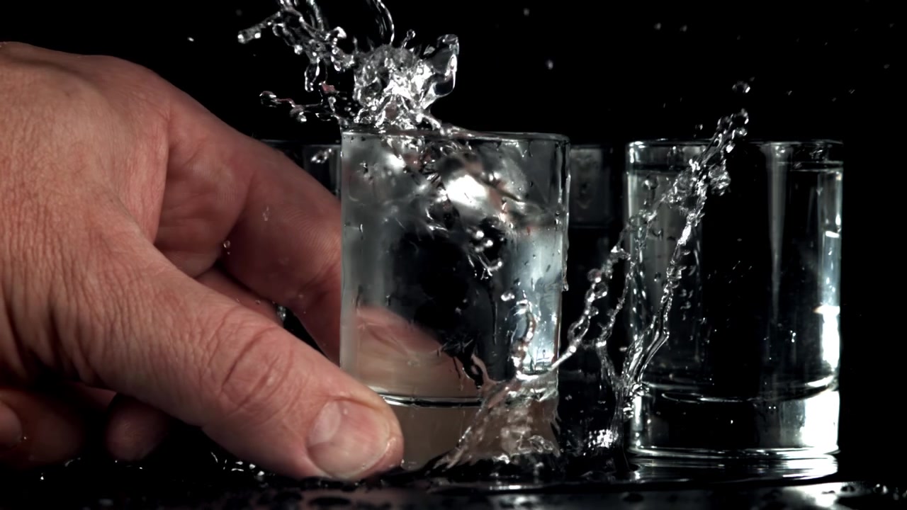 Mano che lascia cadere un cubetto di ghiaccio in un bicchierino da shot con schizzi di liquido al rallentatore