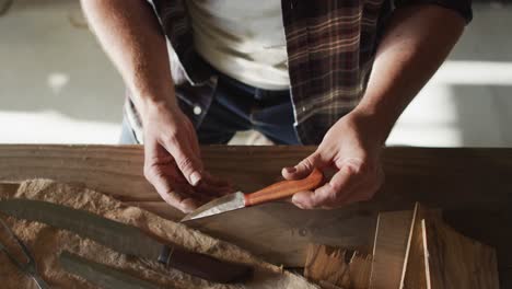 Midsection-of-caucasian-male-knife-maker-in-workshop,-holding-knife