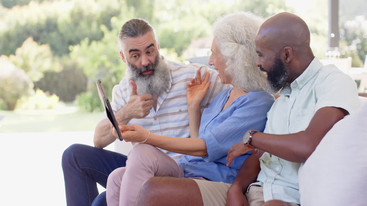 Senior friends laughing and pointing at tablet while sitting on couch