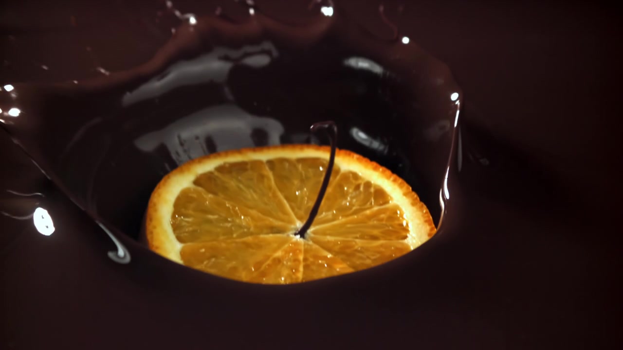 Fetta d'arancia che cade e si tuffa nel cioccolato fuso