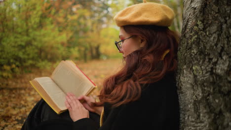 woman wearing yellow beret with red hair cascading over shoulder reads book alone in tranquil autumn forest. immersed in thought, she flips through pages, enjoying peaceful solitude