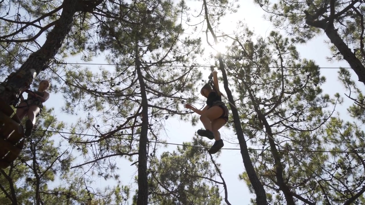 Teenage girl balances across high wire and on to platform in Rope and Tree top Adventure Park