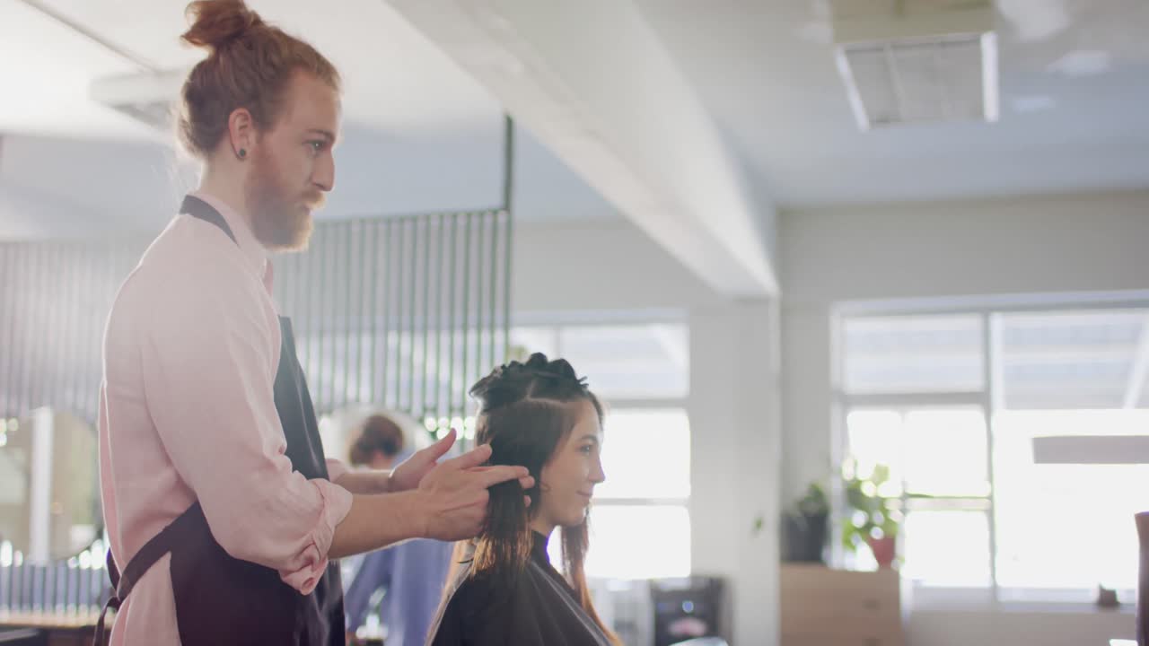 Caucasian male hairdresser with hair bun advising female client at hair salon, in slow motion