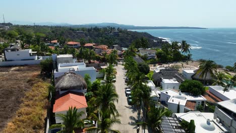 Aerial-view-low-over-a-street-with-palm-trees-and-villas,-toward-the-Carrizalillo-beach-in-Puerto-Escondido,-Mexico