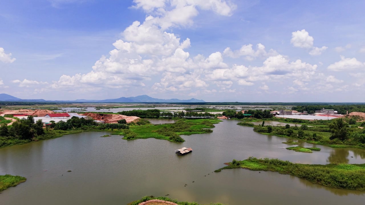 Esto muestra el paisaje de Duc Linh en Lam Dong, Vietnam. Presenta agua, campos verdes y barcos en el río. Es de día bajo un cielo despejado