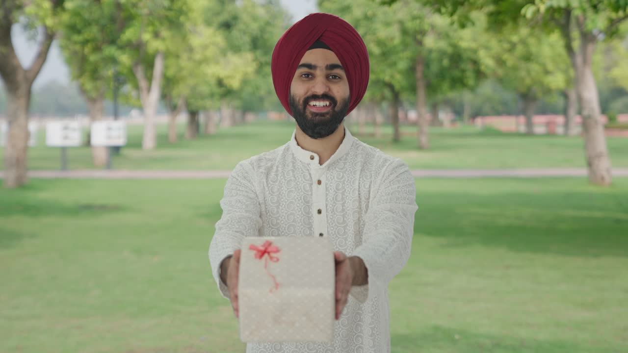 hombre indio sikh feliz dando un regalo en el parque