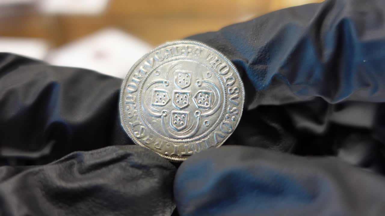 coleccionista examinando una moneda de plata portuguesa de la época medieval