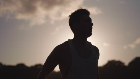 hombre en el parque estirándose antes del ejercicio mientras weing silouetted por el sol