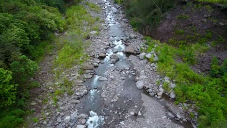 river streaming on rocky bed across green lush vegetation and tropical trees of calm valley on a misty day in hawaii