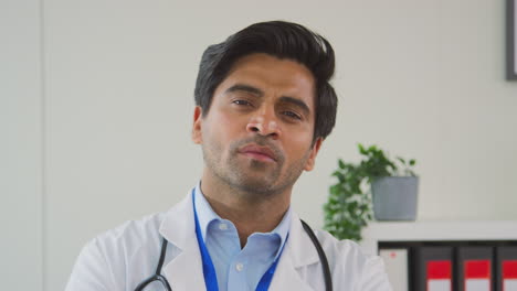 portrait of smiling male doctor or gp with stethoscope wearing white coat standing in office