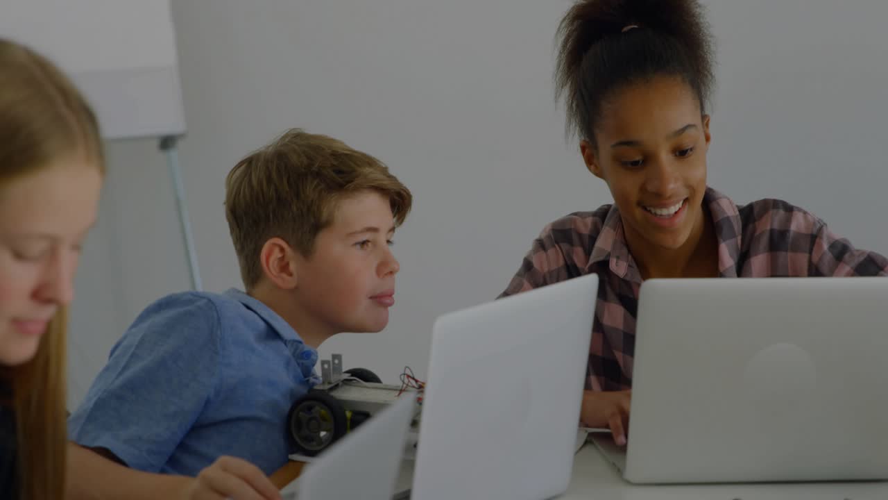 Teen girl typing on laptop and guiding peers in STEM lab, initiating charts intensifying over robot