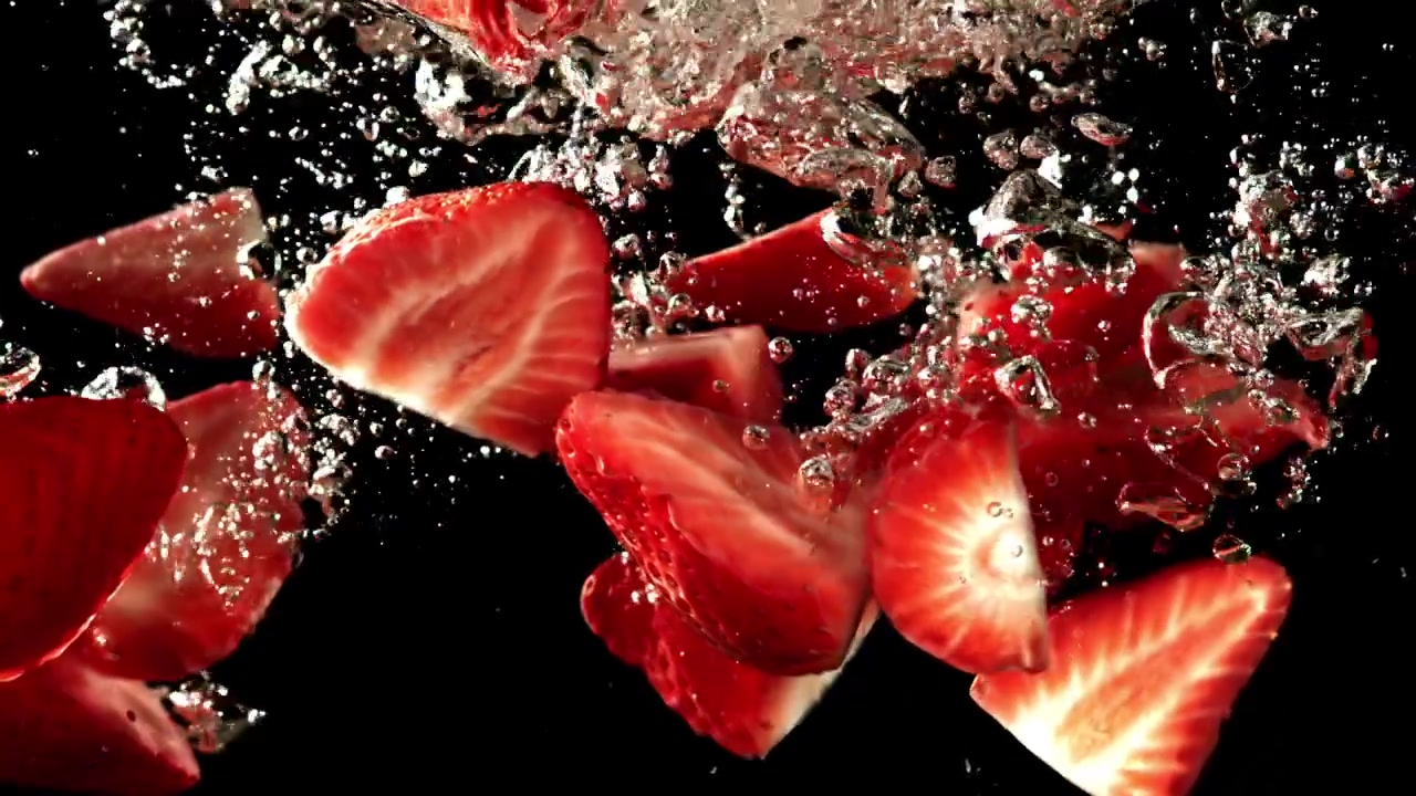 Fragole a fette che cadono nell'acqua con bolle su sfondo nero