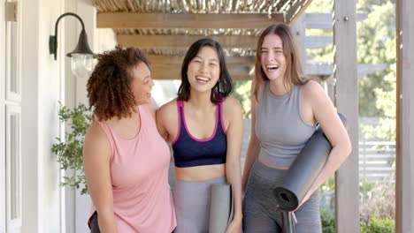 holding yoga mats, three women friends smiling and posing after workout session
