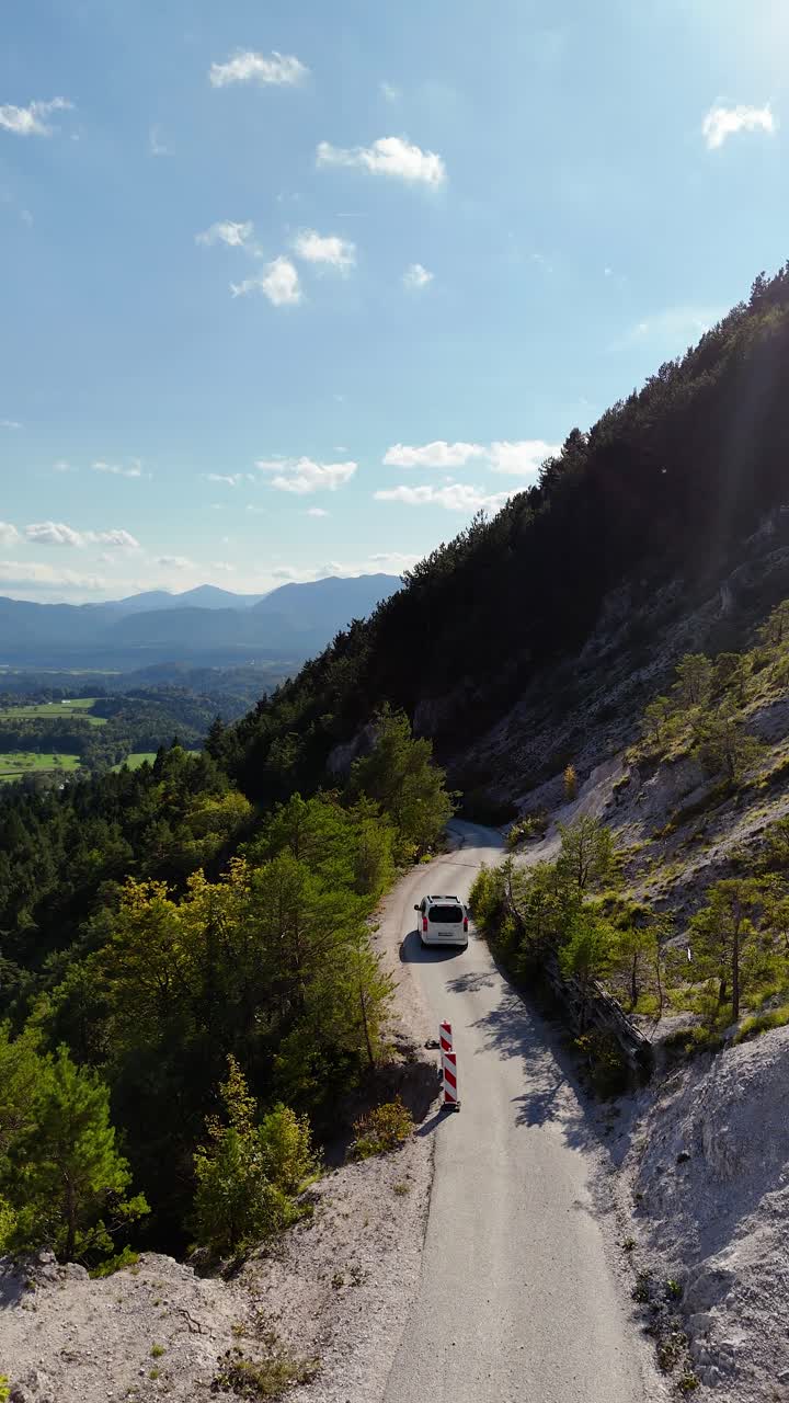 Vertical aerial shot of car driving on narrow mountain road with scenic valley and forest view