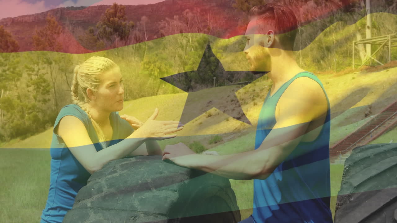In athletic wear, two people talking over large tire with Ghana flag animation
