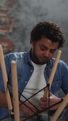 curly haired black man assembles chair sitting on sofa closeup. colleague paints wall in living room. african-american repairmen renovate apartment