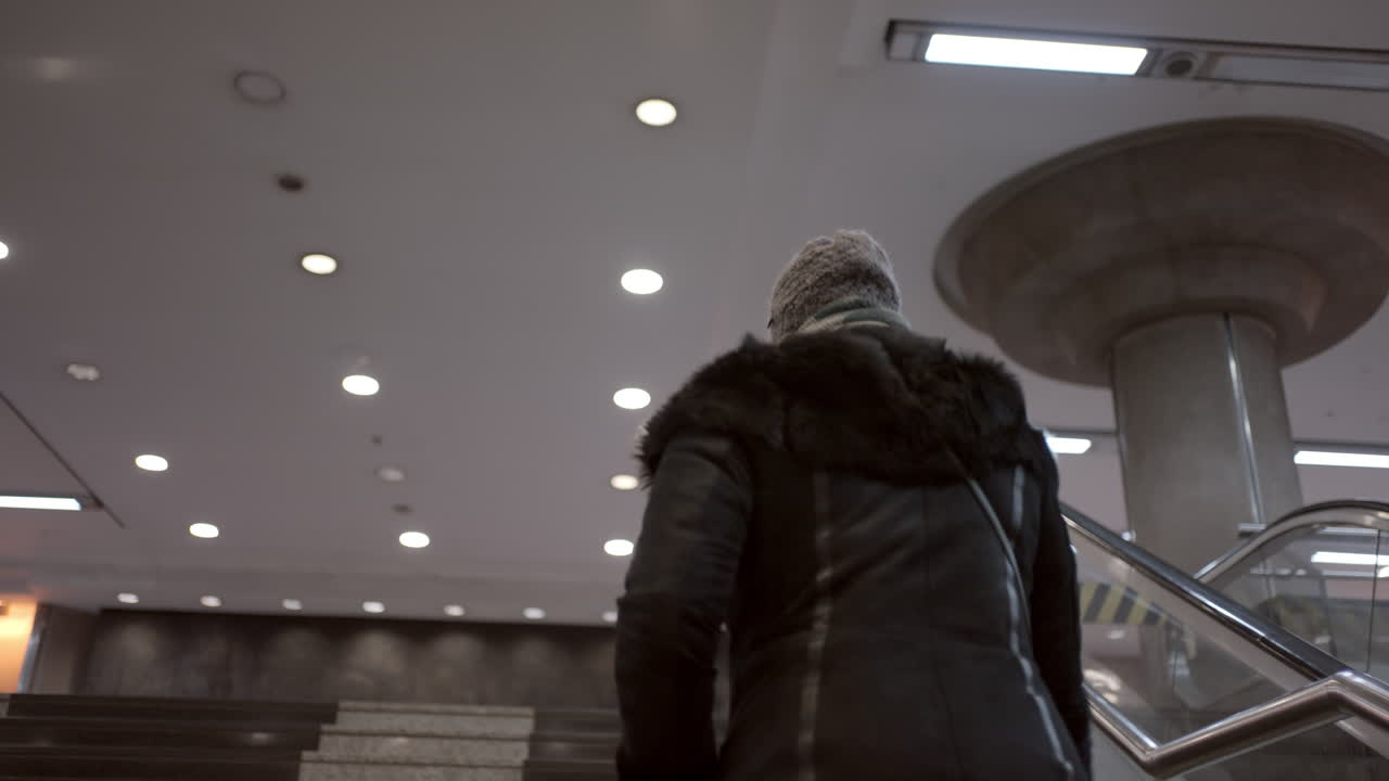Person in a jacket and hat walking on stairs and escalator