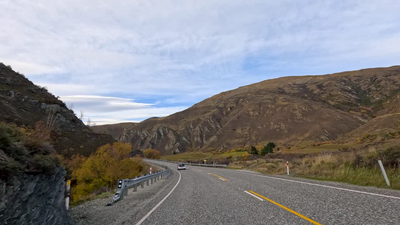 A drive through New Zealand's mountainous roads during autumn, showcasing winding paths, rocky landscapes, and vibrant foliage