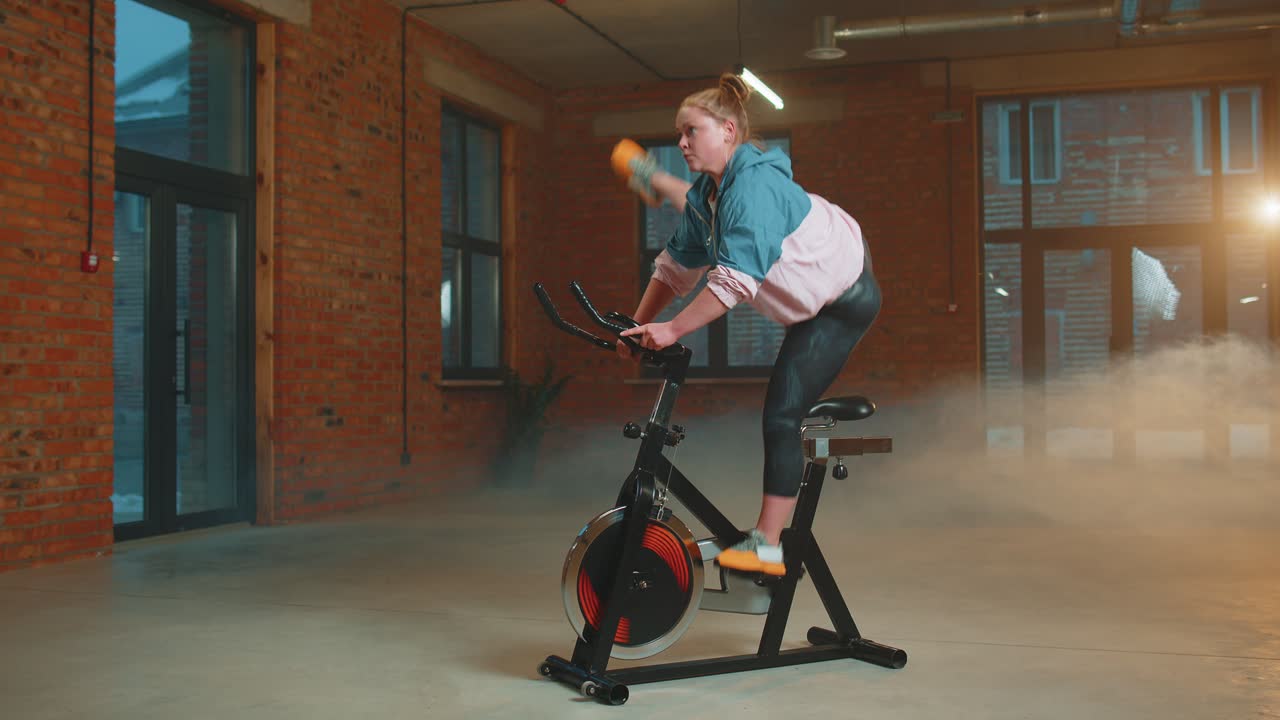 Athletic woman riding on spinning stationary bike training routine in haze gym weight loss indoors