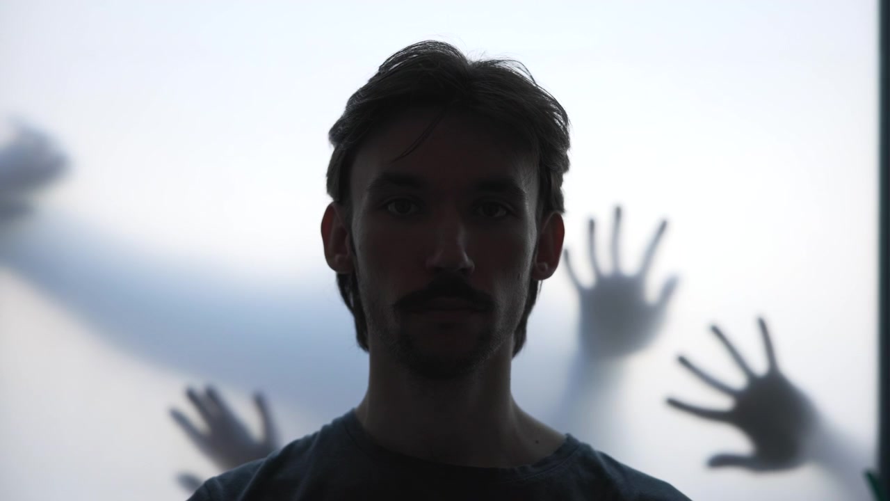 Silhouette di uomo caucasico davanti a vetro smerigliato, ritratto retroilluminato con mani in ombra che premono e si protendono. Media