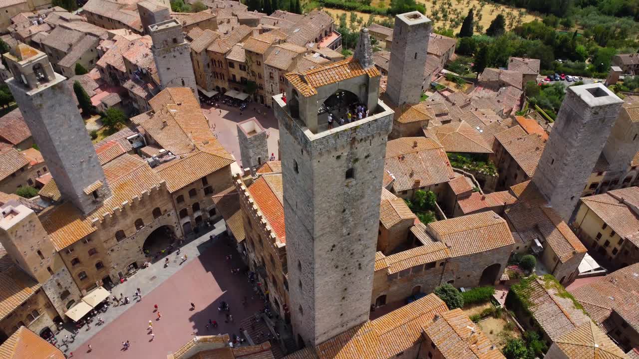 Aerial close-up of San Gimignano’s medieval towers and central square bustling with tourists, captured in vibrant daylight from above.