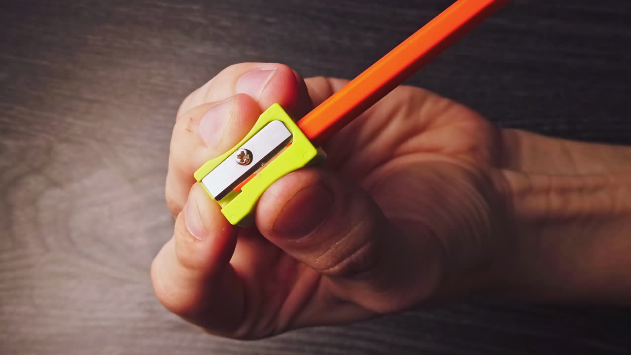 Overhead slow motion of sharpening the pencil in sharpeners on top of the wooden table