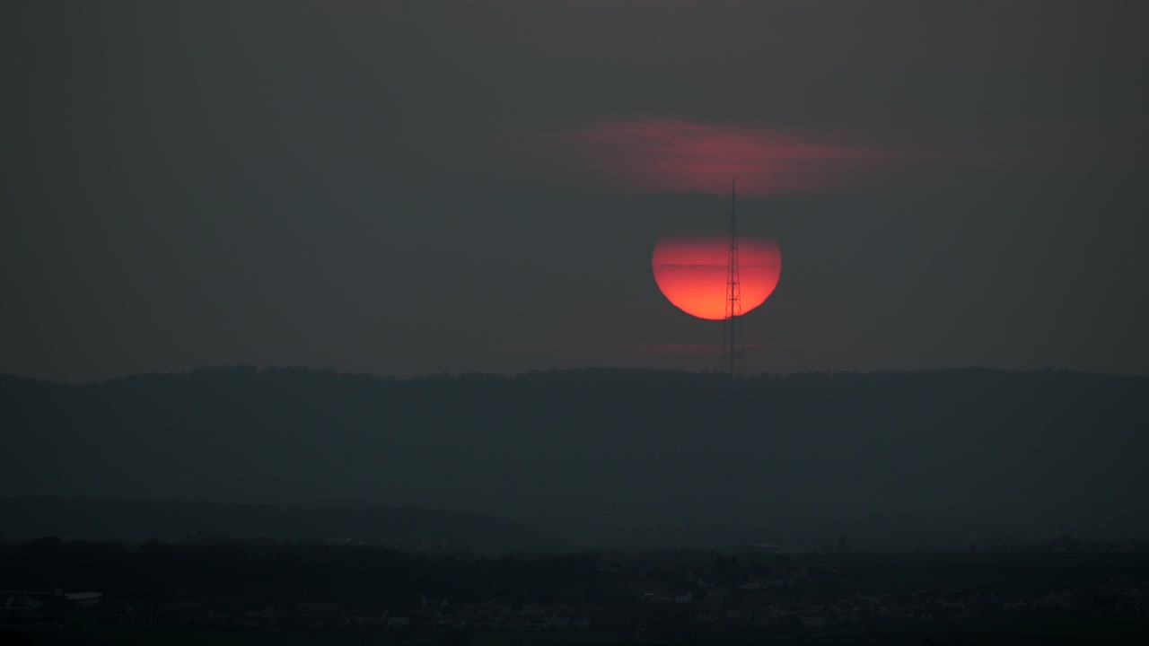 Sunset over a distant landscape time lapse, big dark orange over horizon, tower