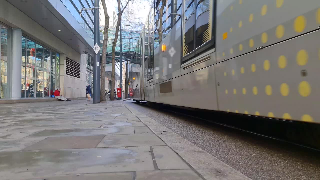 맨체스터 시티 센터를 지나가는 사람들과 함께 거리와 유리 인도교 아래를 여행하는 노란색 메트로링크 트램