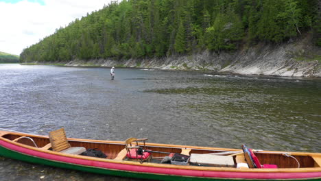 Low-drone-footage-flying-over-canoe-revealing-fisherman-dressed-in-white,-fly-fishing-in-shallow-waters