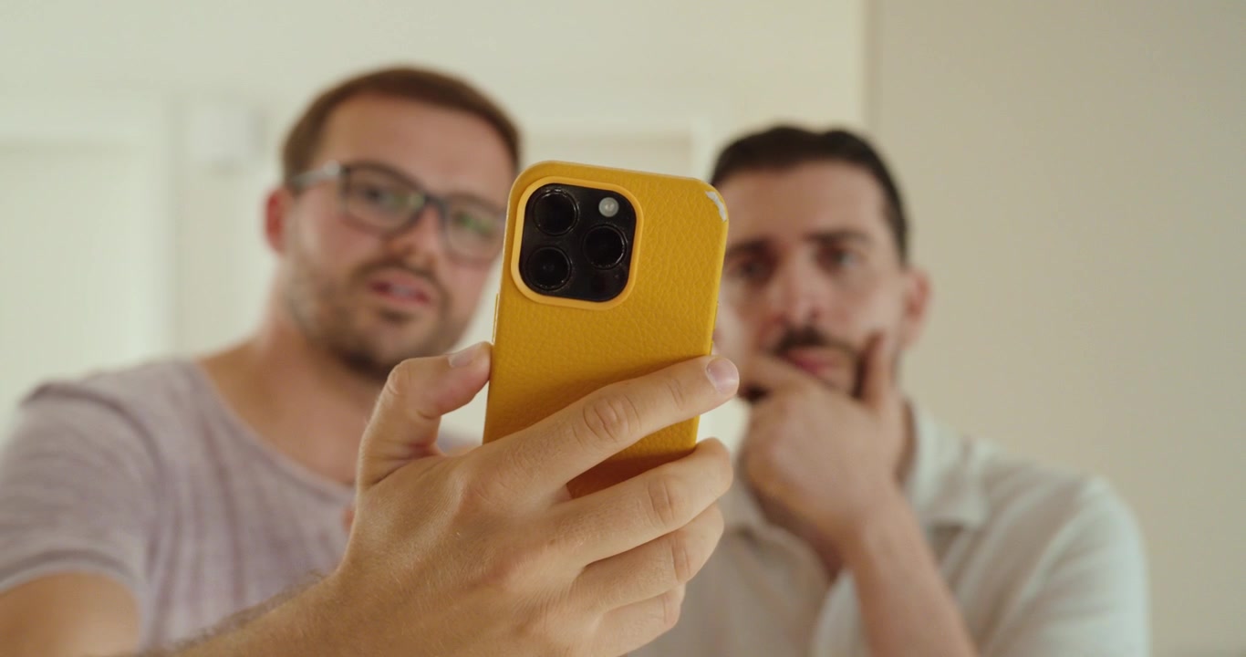 Dva muži se společně dívají na chytrý telefon, diskutují o digitálním obsahu, sdílejí informace a spolupracují na mobilním zařízení.