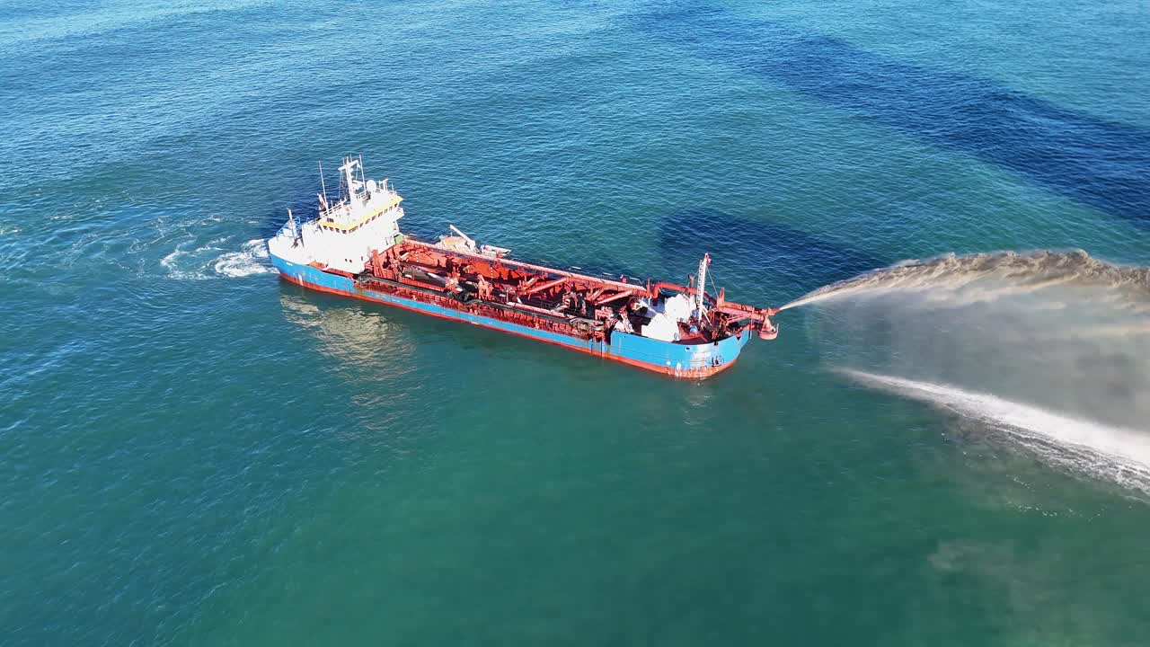 Aerial view of a dredging vessel pumping sand in clear ocean waters under bright sunlight