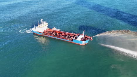 aerial view of a dredging vessel pumping sand in clear ocean waters under bright sunlight