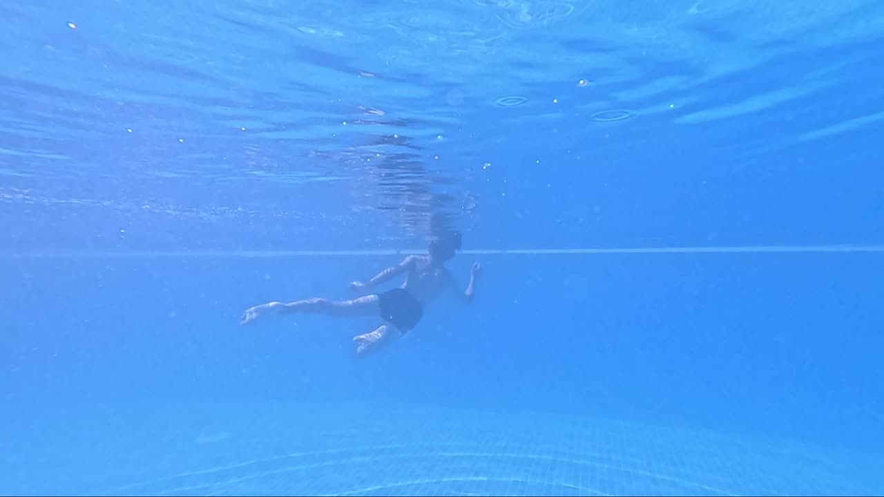 In the tranquil embrace of a shimmering pool, a swimmer glides effortlessly below the surface, exploring the calm and vibrant underwater world around them