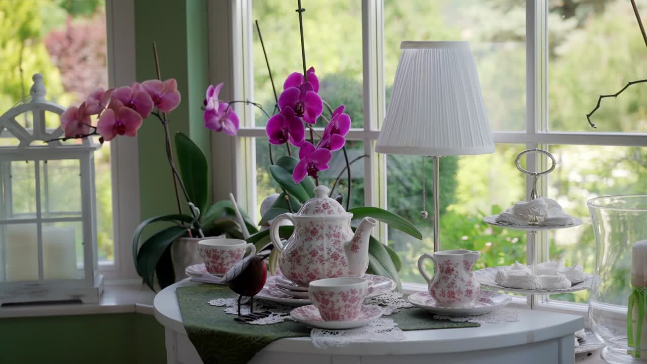 Tea set and blooming orchids on a table near a window