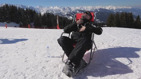 man on a sun lounger in mountains in winter enjoys sunny weather and sunbathing