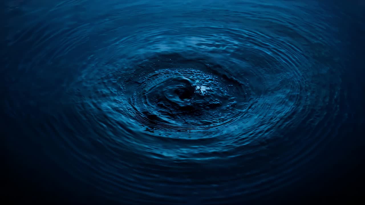 Disturbance appearing at center, water swirling into vortex, concentric ripples on blue-lit water